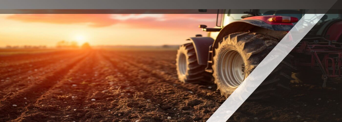 A tractor parked on a freshly sowed field with a beautiful red orange and yellow sunset